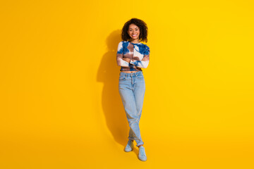 Portrait of a stylish young woman with natural curls posing cheerfully against a vibrant yellow...