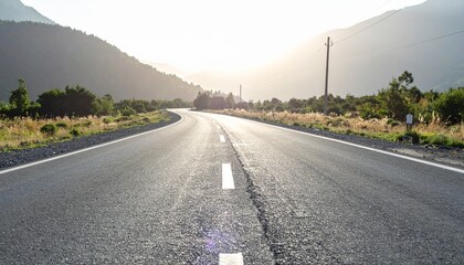 Naklejka premium Scenic asphalt road curves through a lush landscape toward distant mountains and a bright, inviting horizon.