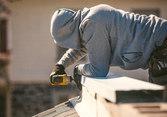 A person wearing a hoodie and work gloves is repairing or installing components on a rooftop next...