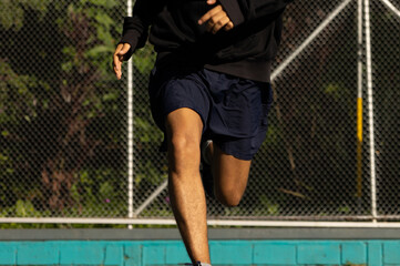 Unrecognizable young man running fast in a straight line in a park in the morning, having a run,...