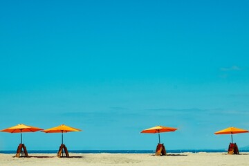 A minimalist beach scene with colorful umbrellas against a clear blue sky.