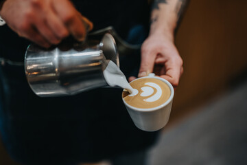 Close-up view of a skilled barista creating latte art by pouring milk into a cup of coffee. The scene captures a moment in the coffee-making process, highlighting expertise and presentation.