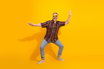 Fashionable mature man with charismatic blond hair and vibrant style posing in playful gestures against a yellow background