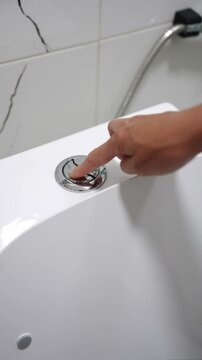 Woman pressing flush button on ceramic white toilet with finger, close up. Hand pressing flush button on modern toilet after using and visiting toilet. Vertical