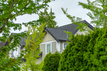 Top of grey stucco luxury house with shingle roof, green trees and nice windows in Spring in Vancouver, Canada, North America. Day time on May 2025.