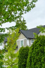 Top of grey stucco luxury house with shingle roof, green trees and nice windows in Spring in Vancouver, Canada, North America. Day time on May 2025.