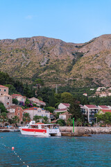 Obraz premium Red and white catamaran sailing near traditional coastal town with mountains rising behind. Summer tourism image.