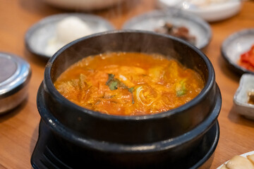 Kimchi Soup served in a bowl, with Korean side dishes served on the table
