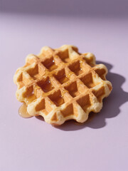 Golden waffle drizzled with syrup on a pastel purple background, perfect for breakfast or dessert inspiration.