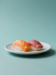 Two pieces of sushi, salmon and tuna nigiri, beautifully plated on a white dish with a teal background, showcasing vibrant colors.