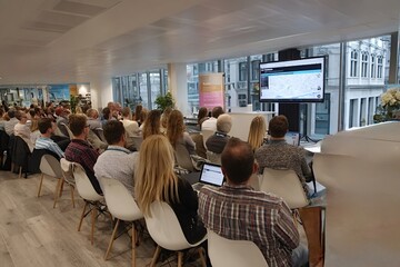 Business people are attending a presentation in a conference room, watching a large screen displaying data and charts, during a business meeting in a modern office