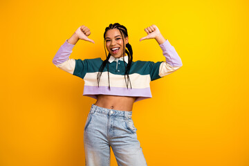 Happy young woman showing confident gesture with both hands against yellow background