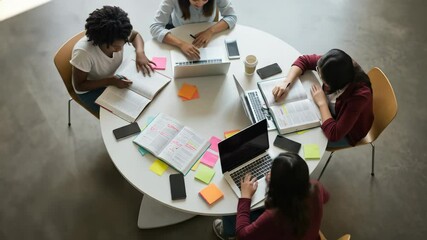Study group of four diverse young adult women intensely collaborating with laptops and books, focused on learning in a modern university setting indoors. - Powered by Adobe
