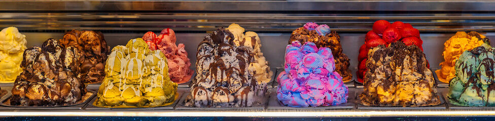 Colorful Gelato Display. Rainbow colored ice cream scoops with chocolate and toppings in a refrigerated showcase. Concept of indulgence, flavor variety, summer sweet temptation