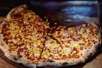 Corn and Ham Pizza. Close-up of sliced pizza topped with ham cubes and sweet corn under melted cheese, food in display case. Concept of fast food, street meal, casual indulgence