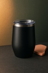 A stylish black tumbler with a lid and small coaster, perfect for a refreshing drink on a warm day. The tumbler has a sleek design and sits on a dark surface.