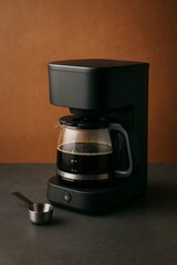 A modern coffee maker with a full carafe of coffee. The coffee maker is black, and there's a small scoop beside it