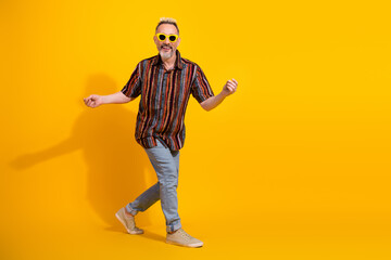 Stylish mature man dancing with charisma in a retro patterned shirt against a vivid yellow background showcasing positivity
