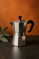 A close-up shot of a coffee pot, with a black handle and top, perfect for brewing rich coffee. The pot has a polished silver appearance. The background shows the details of coffee pot