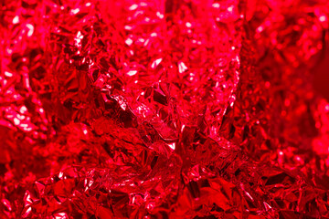 Bright red crumpled foil texture shining in light reveals intricate patterns and reflections