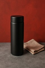 A stylish black thermos and napkin on a grey surface against a red backdrop. Minimalist composition.