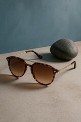 Stylish sunglasses with a tortoise shell design and a simple gray rock placed behind them, suggesting a sense of sophistication and summertime relaxation.