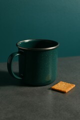 A green coffee mug and a biscuit on a dark background, a minimalist composition, emphasizing the shapes and colors