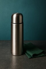 A stylish metal thermos resting on a textured surface. The sleek design suggests both modern functionality and style, appealing to those who appreciate elegant simplicity