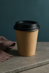 A minimalist shot of a disposable coffee cup on a stone surface, with a dark teal background