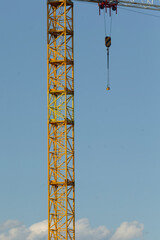 A tall construction crane, featuring a prominent hook, looms against a clear blue sky. This...
