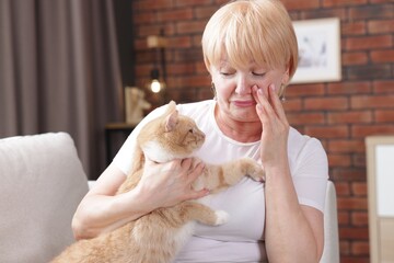 Senior woman suffering from allergy with her cat on sofa at home