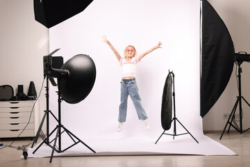 Little girl jumping on white background in photo studio with professional equipment