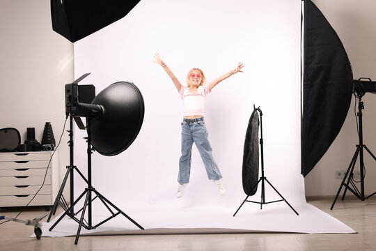 Little girl jumping on white background in photo studio with professional equipment
