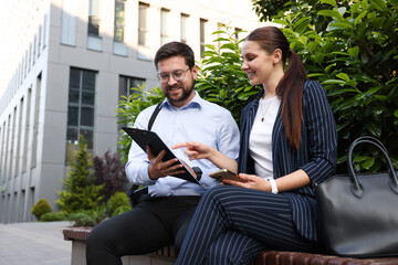 Happy coworkers discussing something on bench near office building
