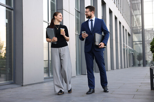 Happy coworkers with smartphone and coffee discussing something near office building