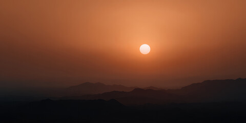 Sunset over hazy mountain ridge with orange sky creates serene atmosphere