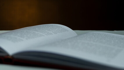 Open book with blurred text under warm light against black background, moody still life concept...