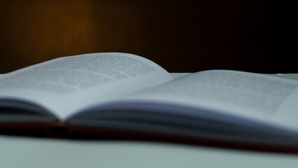 Open book with blurred text under warm light against black background, moody still life concept...