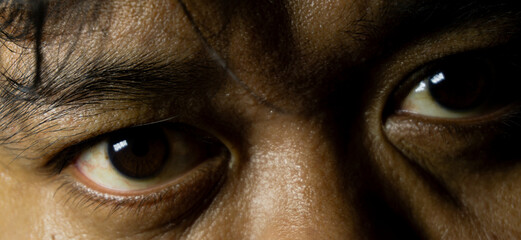 Close-up of Indonesian man's eyes with dark brown irises, intense eye contact and clear detail,...