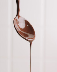 melted chocolate dripping from a silver spoon against a clean white studio background, rich...