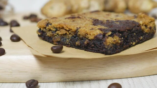 Blondie and brownie layered dessert resting on baking paper atop a wooden board, adorned with coffee beans and softly blurred ginger cookies, creating an inviting and indulgent scene