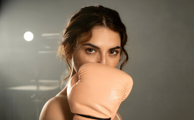 Studio Strength: Confident Young Woman in Peach Boxing Gloves Posing with Fierce Eyes Under Dramatic Lighting