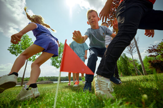 Group of children engage in capture the flag beneath a bright sky within a park. Concept of childhood competition, active outdoor play, summer group activities