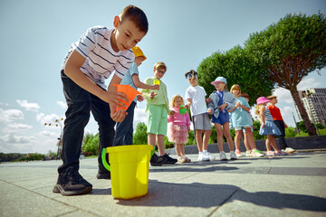 Children participate in outside activities, utilizing buckets and cones to explore and play. Concept of interactive learning and enjoyment in a natural setting.