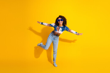 Cheerful young woman in casual attire posing energetically against a vibrant yellow backdrop expressing joy and style