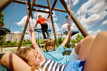 Youngsters happily engage in play on a wooden climber at a playground beneath a cloudless sky,...