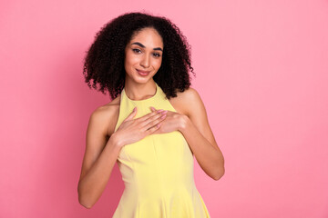 Charming young woman with curly hair in a yellow dress posing against a pink background, expressing...