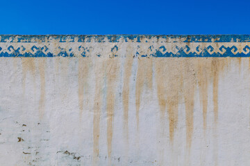 Weathered white wall with blue painted Kyrgyz ornament and water stains outdoors