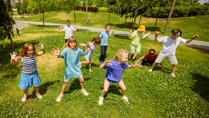Children happily engage in play in a park illuminated by sunlight, surrounded by lush green grass...