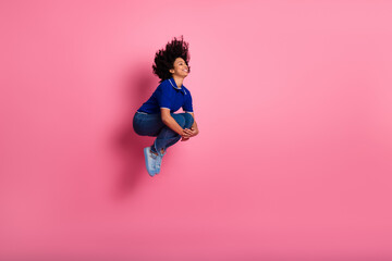 Energetic young woman joyful in mid-air against a vibrant pink backdrop, showcasing stylish casual...